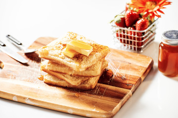 Toasted crumpets with honey drizzled over them and strawberries in the background.