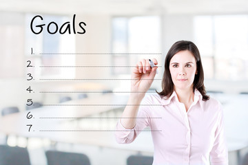 Business woman writing blank goal list. Office background. 