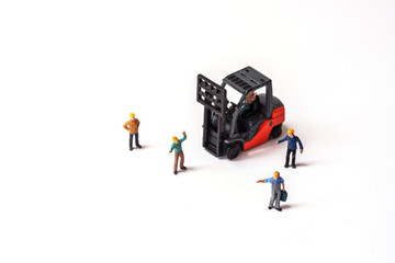 selective focus of miniature worker holding bag and standing front of forklift machine, on white background.