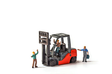selective focus of miniature worker holding bag and standing front of forklift machine, on white background.