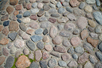 Ancient paving stones. The cobblestones of the ancient city. Natural surface roads. Background and texture of the stones. Round stones of the street.