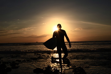 Surfer Walks Down Beach at Sunset - obrazy, fototapety, plakaty