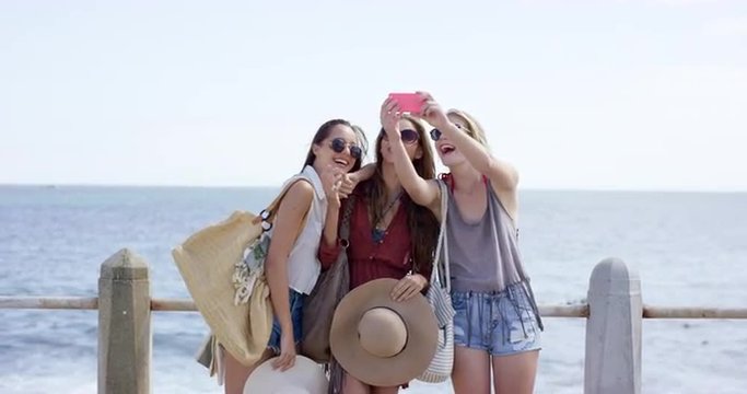 Three young woman on summer vacation taking selfie on beach promenade wearing denim shorts