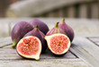 Whole figs and one fig sliced in half on top of a teak garden table. Focus is on the sliced fig.
