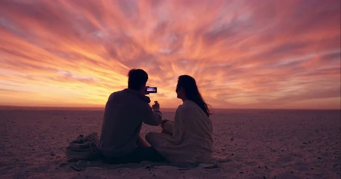 Happy romantic couple taking photograph of sunset using mobile phone camera wide shot on RED DRAGON