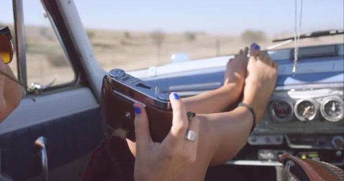 beautiful girl taking photos with vintage camera on road trip in convertible car