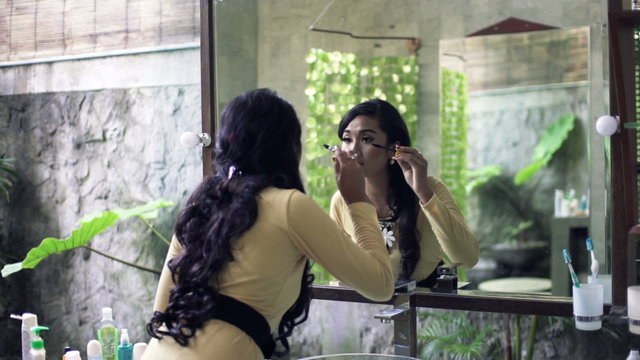 Pretty, asian woman applying mascara eyelash in front of the mirror in bathroom
