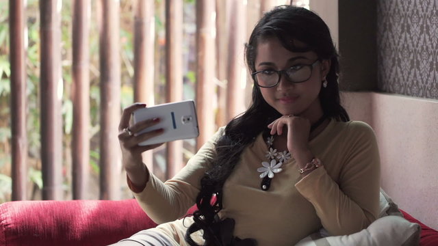 Young woman taking selfie with cellphone on sofa at home 
