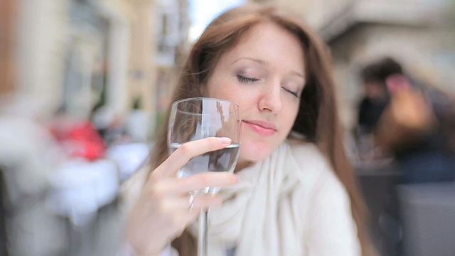 A young woman is drinking a glass of water in the street cafes.