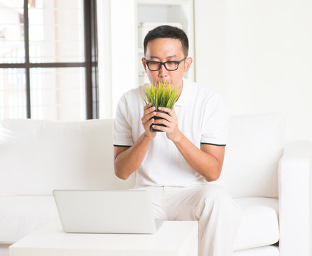 Casual Asian Man Sniffing Grass In Livingroom