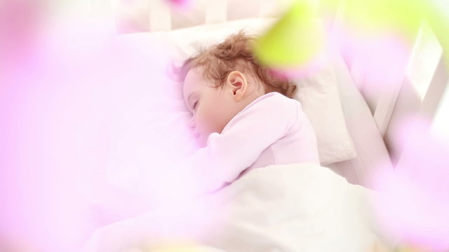 Baby is sleeping in her crib with toys.
