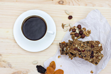 Homemade rustic granola bars with dried fruits and handmade packaged and cup of coffee on wooden background