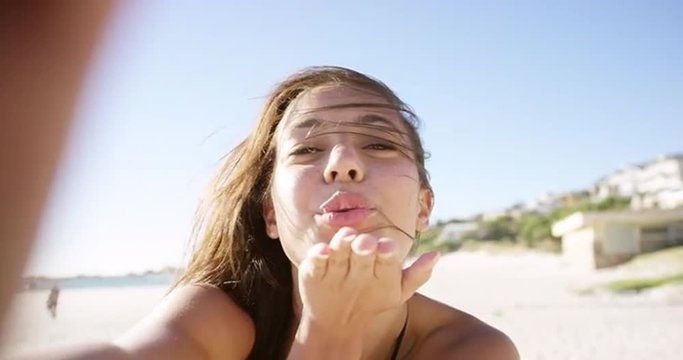 beautiful young woman taking selfie on beach at sunset blowing kiss