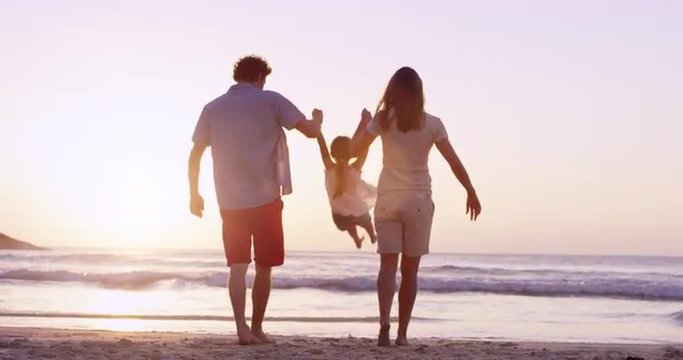 Happy family on the beach holding hands swinging little girl around at sunset on vacation