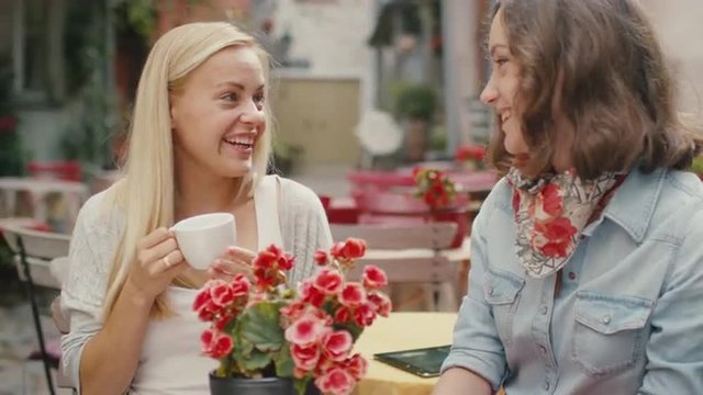 Two Girls Have Conversation in Outdoor Coffee Shop