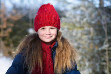 Portrait of a little smiling girl in winter hat in snow forest