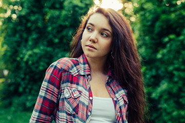 Brown hair girl sitting on the grass in the park and posing to the picture.