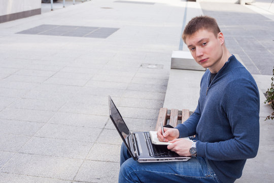 College student learning over the bench with laptop.