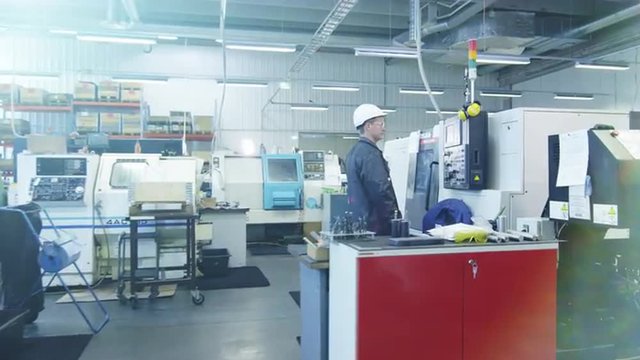 Factory Worker in Hard Hat is Setting Up CNC Lathe Machine
