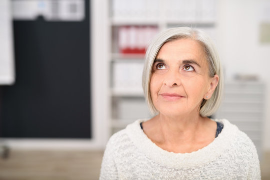 &auml;ltere frau im b&uuml;ro schaut in gedanken nach oben