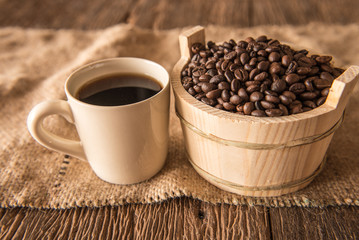 Coffee beans in wooden bowl and coffee cup on wooden background.
