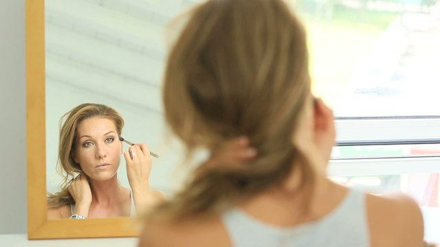 Beautiful woman in front of mirror putting makeup on
