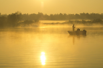Obraz na płótnie Canvas Wędkarz na łodzi łowiący w mglisty poranek nad rzeką