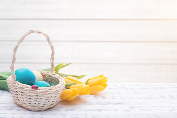 Beautiful Easter eggs in a basket. Delicate yellow spring tulips. Spring Easter holidays. Wooden board rustic