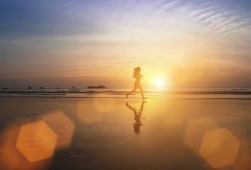 Silhouette of a young jogger girl running through the surf at amazing sunset.