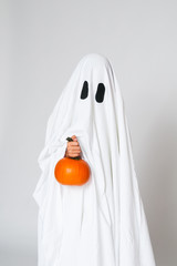 young child dressed as a ghost holding a pumpkin for halloween