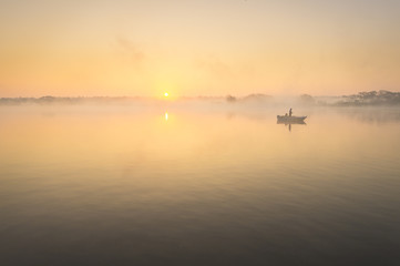 Wędkarz na łodzi łowiący w mglisty poranek nad rzeką - obrazy, fototapety, plakaty