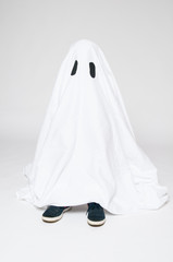 child dressed as a halloween ghost with his feet showing beneath the sheet