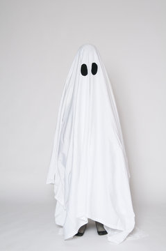 child dressed as a halloween ghost with his feet showing beneath the sheet