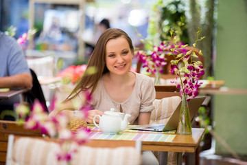 Young beautiful woman sitting in cafe and drinking coffee. Working with the laptop on terrace.

