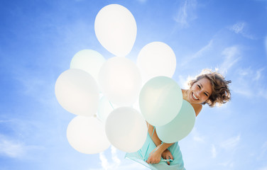 Young girl in a dress, smiling and laughing holding balloons aga