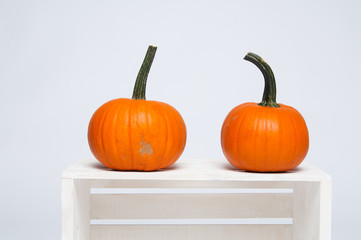 two bright orange pumpkins on a white crate