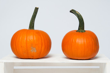 two bright orange pumpkins on a white crate