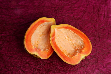 A papaya fruit cut in half , and placed opposite to each other and photographed over maroon background paper