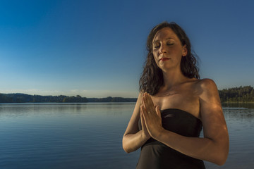 Junge Frau stimmt sich meditativ auf Yoga am See ein