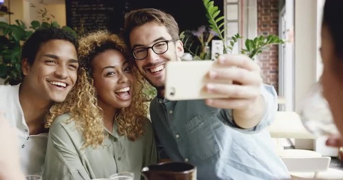 Mixed race group of friends taking selfie photograph in cafe