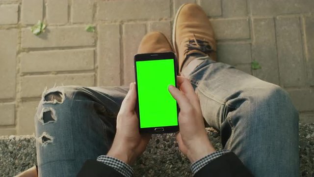 Man is Using Android Phone on Lap Outdoors at Sunny Day. POV