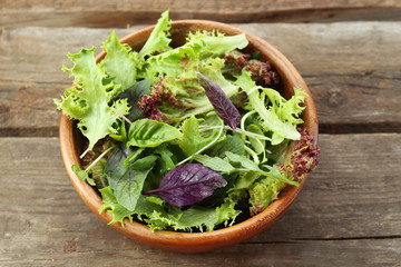 Fresh mixed green salad in bowl on wooden table close up