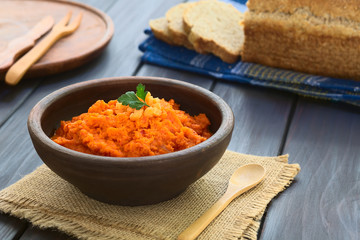 Carrot and red bell pepper spread in rustic bowl garnished with parsley leaf, wholegrain bread in...
