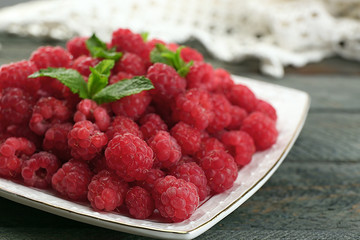 Sweet raspberries on plate on wooden  background