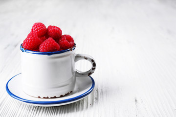 Fresh red raspberries in cup on wooden background