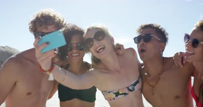 Mixed race group of friends taking selfies on the beach using phone camera