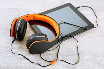 Headphones with tablet on wooden table close up