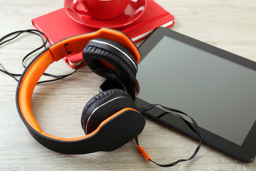 Headphones with tablet and notebook on wooden table close up