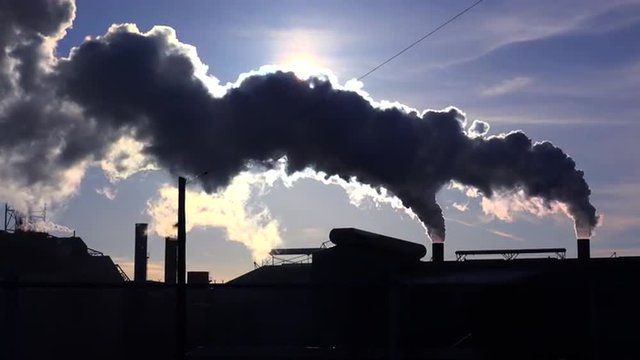 Global warming is suggested by shots of a steel mill belching smoke into the air with sun background.