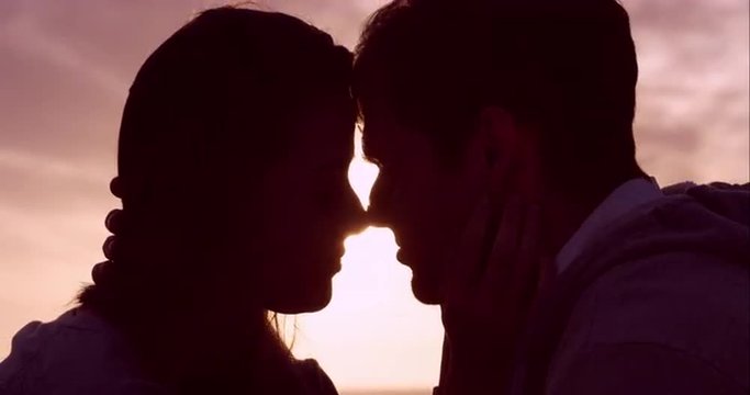 Happy loving couple kissing at sunset showing emotional intimacy touching hugging and cuddling